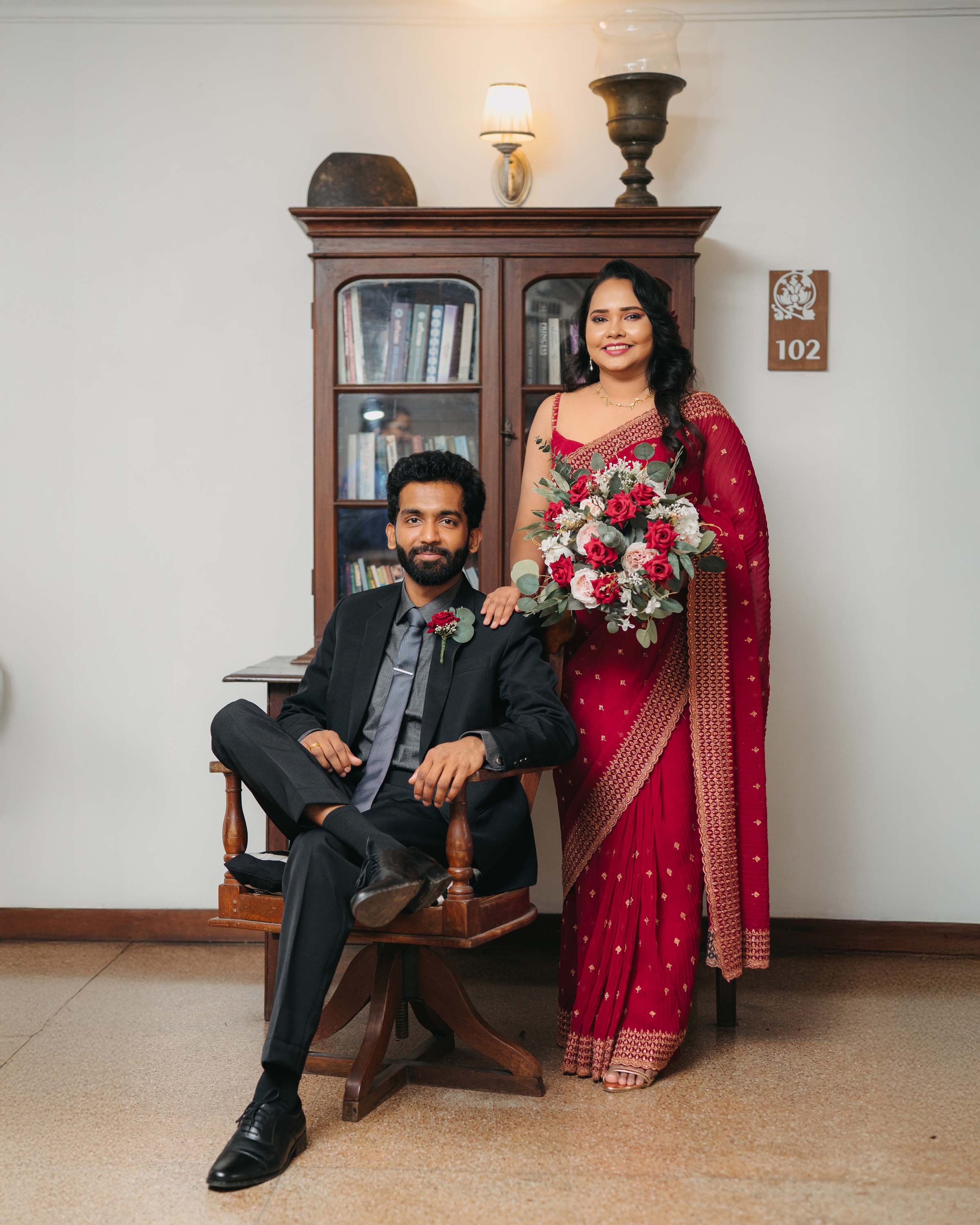 Elegant Sri Lankan wedding couple portrait in maroon saree and suit inside a vintage studio.